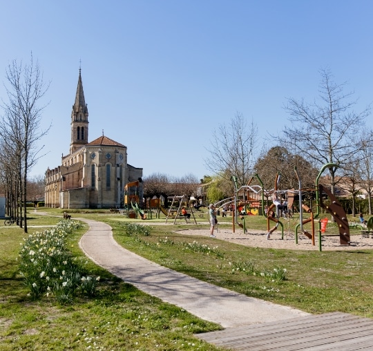 Esplanade et aire de jeux pour enfants au pied de l'église de Sainte-Hélène avec parterres fleuris